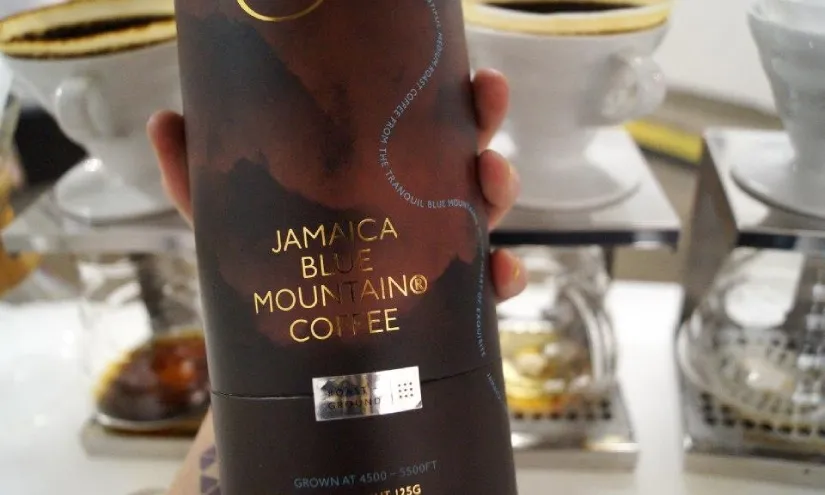 Coffee farmer with a bag of Blue Mountain Coffee, QR code visible on packaging.